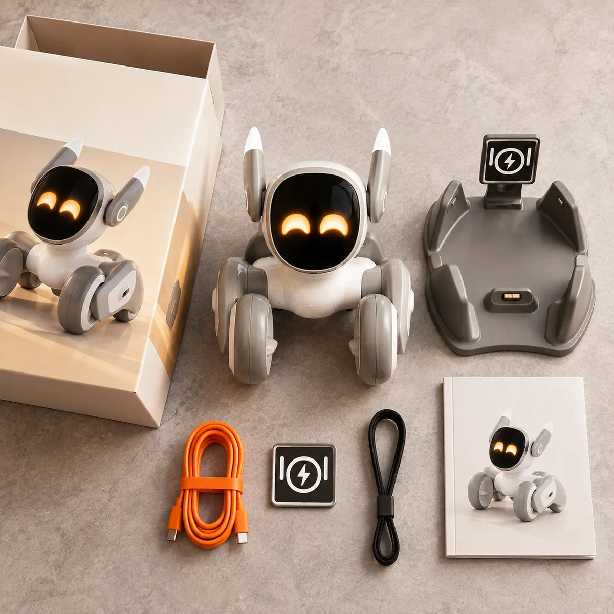 A smart robot toy set arranged on a light gray surface, including a white and gray robot with glowing orange eyes, a charging dock, an orange cable, a black cable, a small square accessory, a booklet, and part of its box.