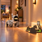 A small white and gray wheeled robot toy with glowing yellow eyes is positioned on a polished wood hallway floor, facing a dark gray target stand with a light beam trail connecting the two. The scene is set in a warmly lit home interior.